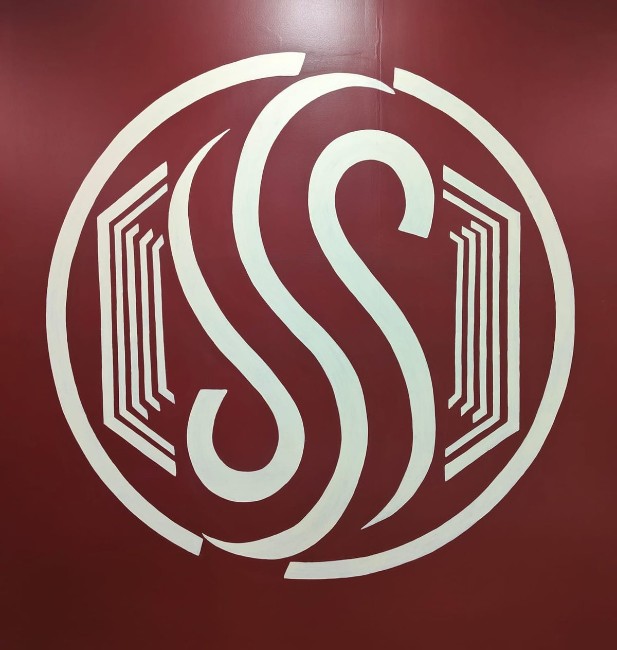 Large hand-painted circular monogram logo on a maroon wall