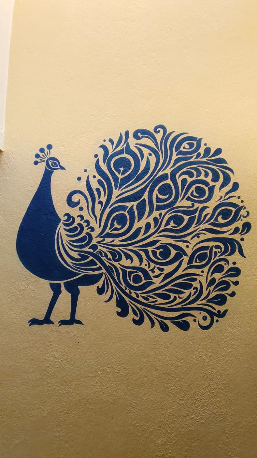 Indigo stencil-style peacock mural on a mustard wall