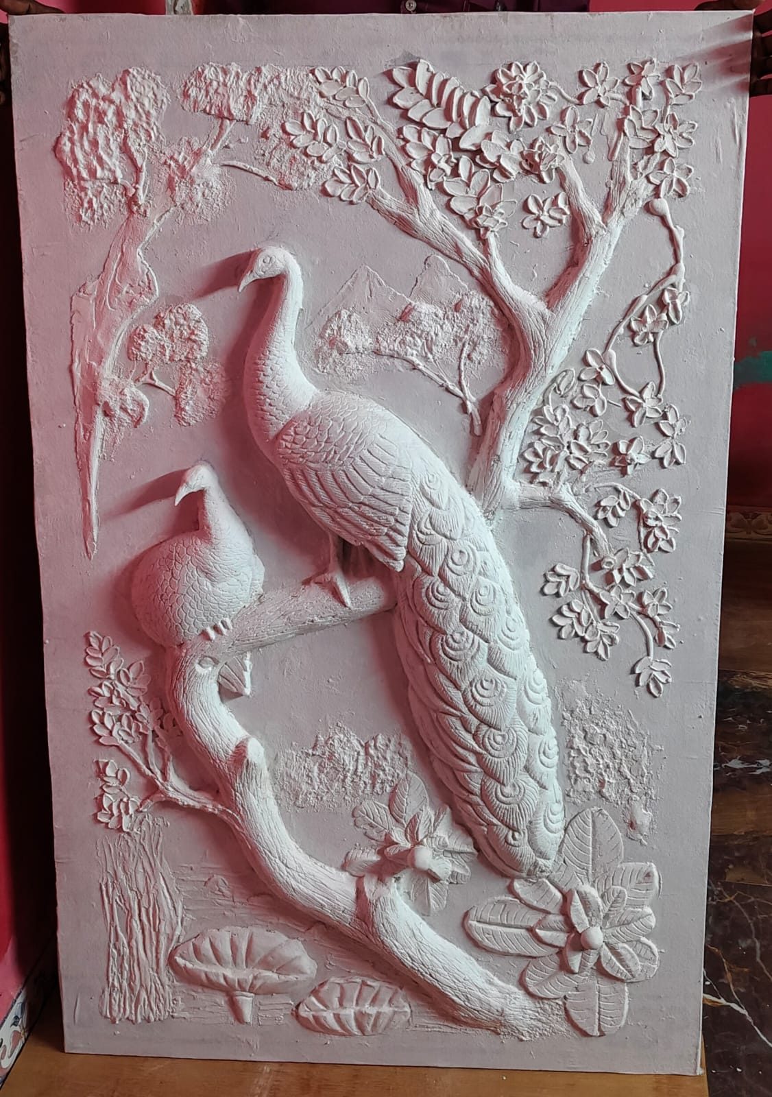 White plaster relief of two peacocks beneath a blossoming branch