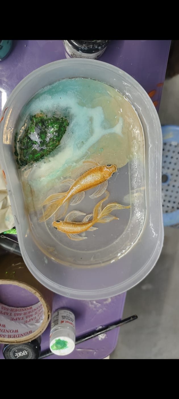 Resin art piece in a mould showing two golden koi fish swimming over a green mossy rock