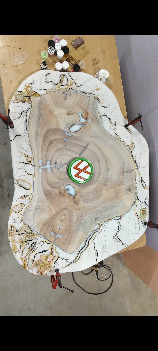 Live-edge wood slab table in progress with a white and gold marbled epoxy resin border and inlaid emblem