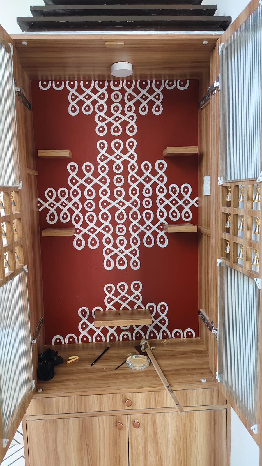 Home pooja room cabinet interior hand-painted with a white kolam pattern on maroon